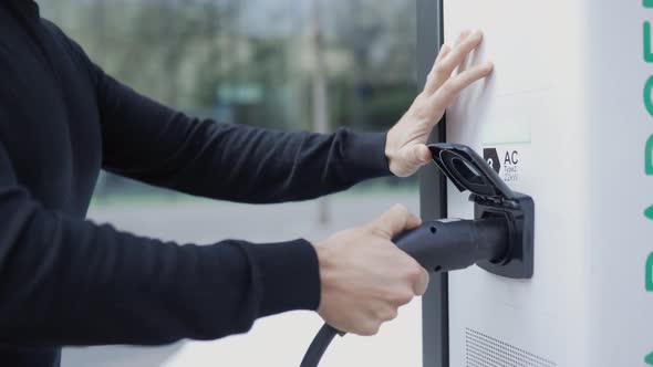 Woman connecting charging plug to electric vehicle charging station