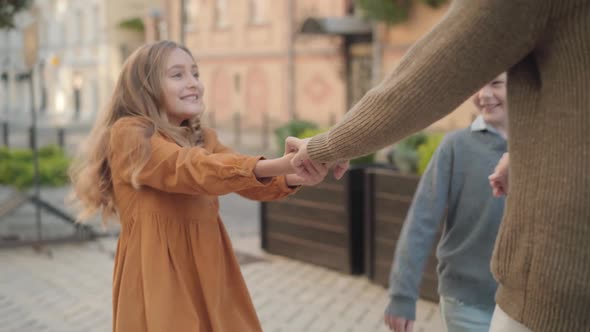 Portrait of Joyful Caucasian Girl and Boy Pulling Hands of Senior Unrecognizable Grandfather