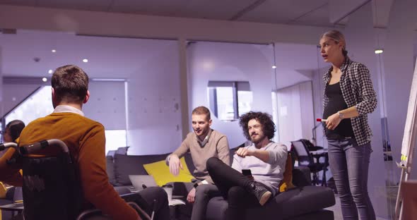 Disabled Businessman in a Wheelchair at Work in Modern Open Space Coworking Office on Team Meeting