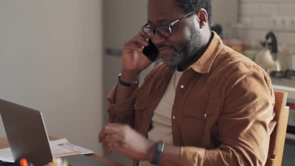 Concentrated man working on laptop and talking while his daughter doing homework