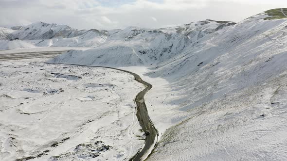 Aerial of Car Driving on Dirt Road Along the Snow Covered Mountains in Iceland