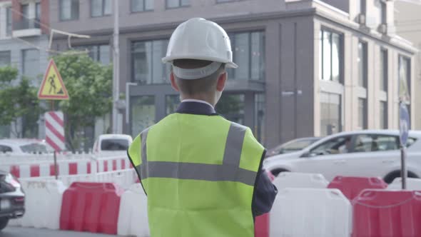 Little Boy Wearing Business Suit and Safety Equipment and Constructor Helmet Standing on a Busy Road