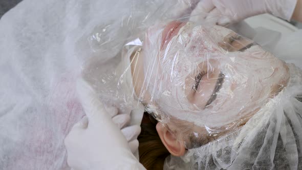 Girl Beautician Wears a Transparent Film on the Patient Lying