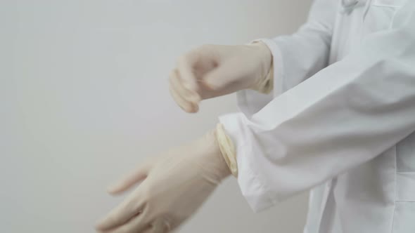 Young Female Doctor in White Coat Demonstrates How To Put Protective Gloves. COVID-19