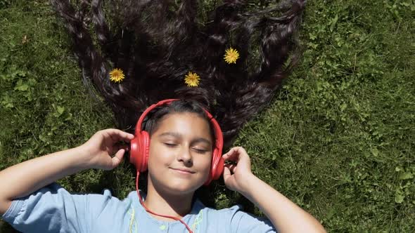 The Girl Lies on the Grass in the Park and Listens to the Music in the Headphones