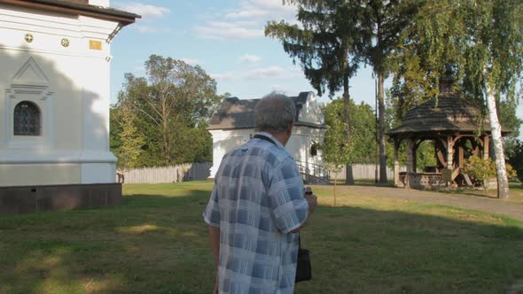 Pensioner Holds Black Camera and Takes Photo in Museum Park