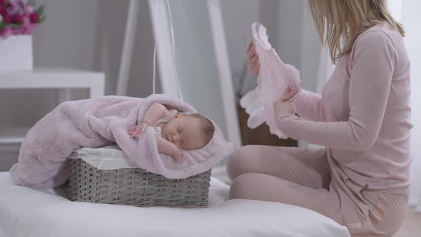 Cute Sleeping Baby Girl in Basket with Unrecognizable Woman Admiring Pink Suit