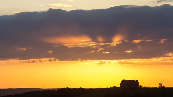 Timelapse of sunset with orange and pink fast moving clouds and yellow sun beams.