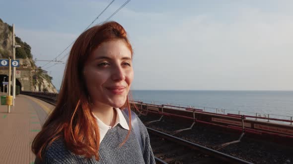 Girl Smiles While Waiting for the Train at the Station Near the Sea