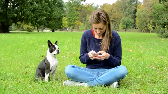 Young Attractive Happy Woman Writes Messages on the Smartphone and Ignores Her French Bulldog