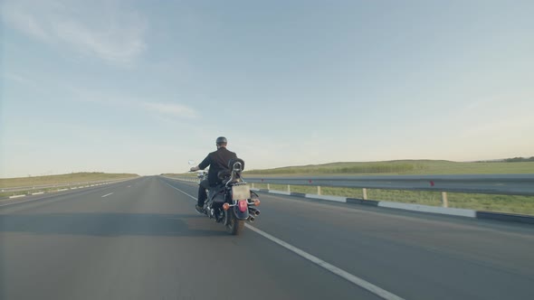 Confident Male Biker in Black Leather Jacket and Helmet Rides Along the Highway on a Black