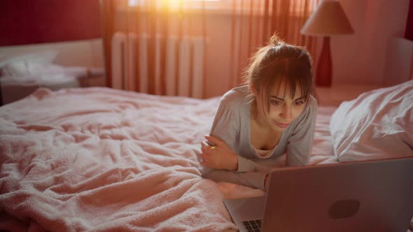 Young Woman Lying on Bed at Home and Watching Laptop Computer Browsing on Internet