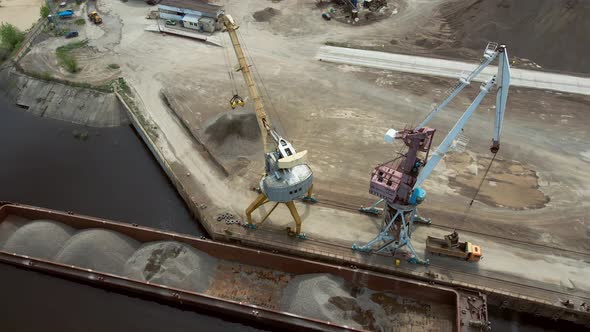 Huge Harbor Cranes on the River Bank Unload Rubble From a Barge