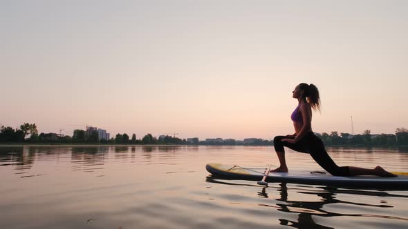 Young Woman Doing Yoga on SUP Board at Sunset