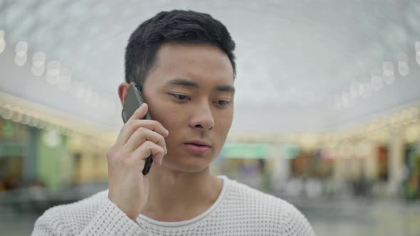 Close Up of Asian Male Talking on Phone on Shopping Center Background