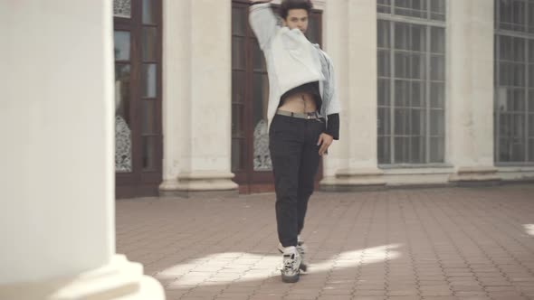 Wide Shot of Millennial Caucasian Man Dancing on Sunny Day Outdoors with Urban Columns Passing at