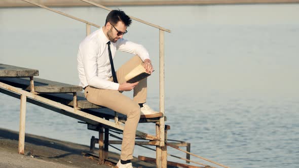 Businessman Relaxing And Enjoying Near River Resting Holding Book. Man Sitting And Reading Diary.