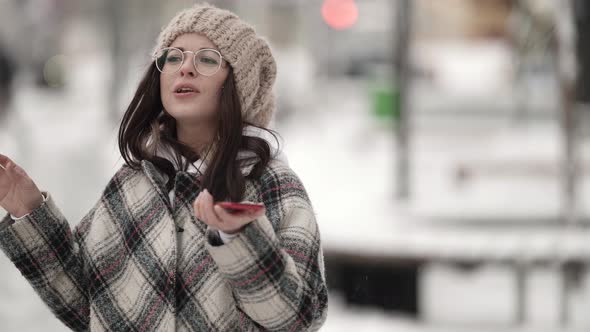 Portrait of a Beautiful Young Darkhaired Woman in Round Glasses and a Plaid Coat Walking on a Snowy