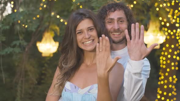 Portrait of Happy Young Caucasian Couple Showing Wedding Rings and Smiling at Camera. Positive