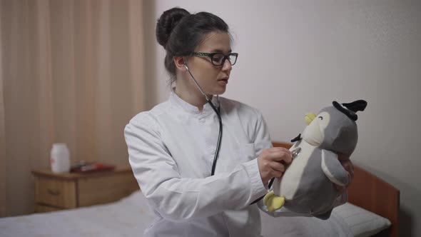 Young Medical Student with Stethoscope Practicing on Toy Sitting on Bed at Home