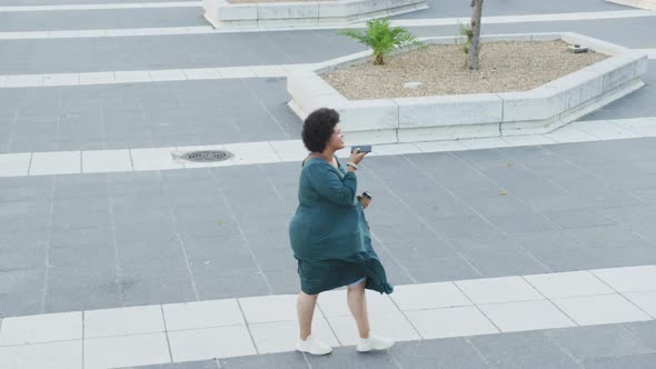 Happy plus size biracial woman talking on smartphone and walking