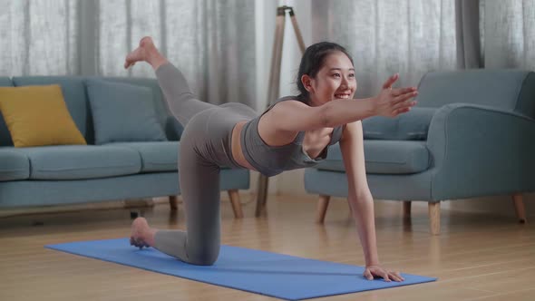 Asian Athletic Female In Sports Clothes Doing Yoga In Balancing Table Pose On The Mat At Home