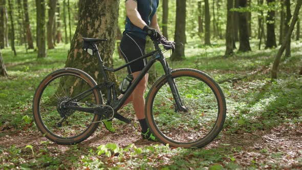 A Cyclist is Walking with a Bicycle Along a Forest Path