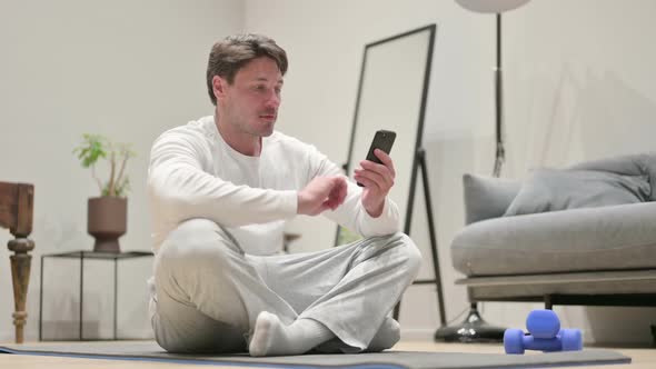 Man Using Smartphone on Yoga Mat at Home