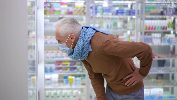 Side View Senior Caucasian Man Leaning at Shelves in Pharmacy Choosing Efficient Medication on