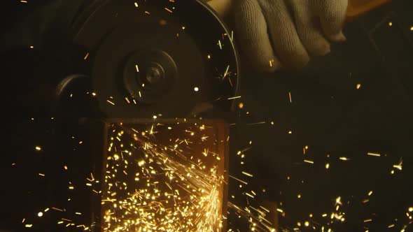 Industrial worker using an angle grinder and cutting a metal square pipe