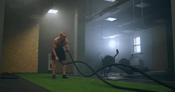 Fitness Man Exercising with Battle Rope Abandoned Warehouse. Tough Man Working Out in Cross Training