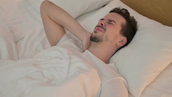 Tired Young Man Having Neck Pain in Bed