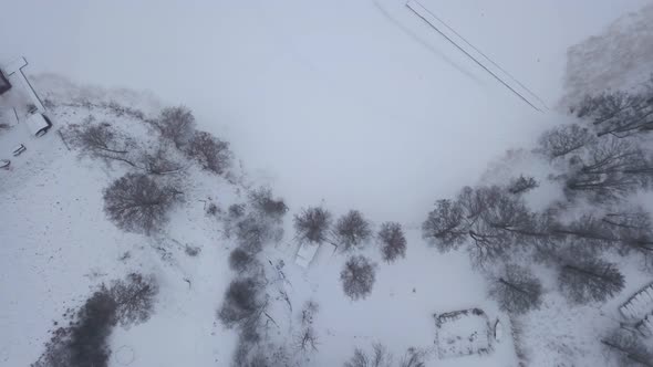 Bird's eye view with slight zoom in on edge of frozen lake that is surrounded by deciduous trees.