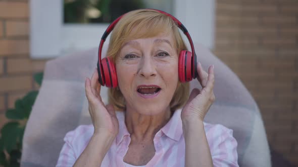 Headshot Portrait of Joyful Senior Caucasian Woman in Headphones Singing Looking at Camera Smiling