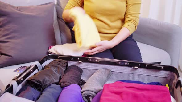 Woman preparing suitcase with clothes for travel. Booking a ticket using a credit card.
