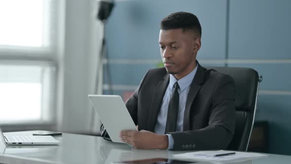 African Businessman Celebrating Success on Tablet in Office