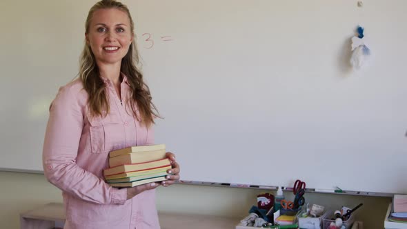 Female teacher holding stack of books in school