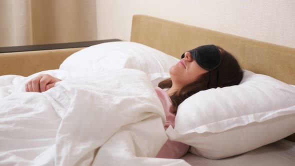 Young Woman Wearing Sleeping Mask Lies Relaxed in Modern Bed