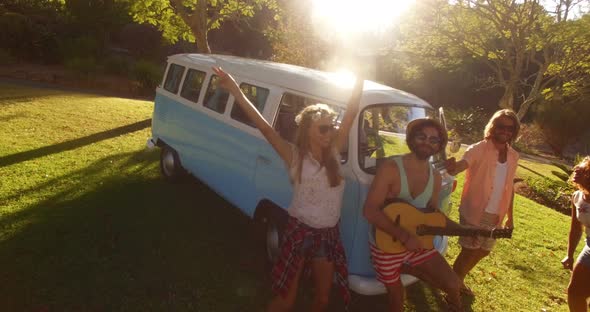 Man playing guitar in campervan and friends dancing beside him