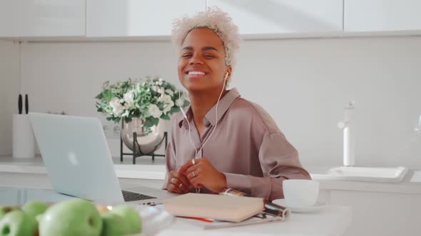 African American Woman Puts on Headphones and Looks at Camera Sits at Kitchen alt