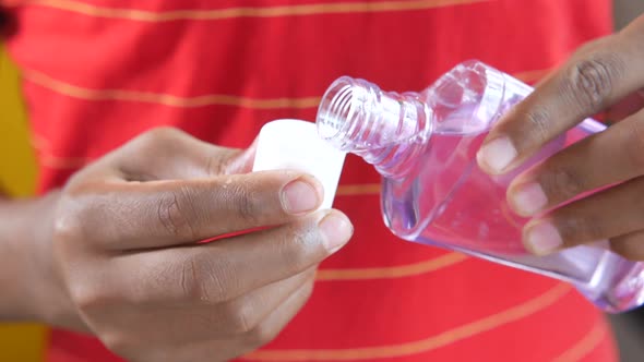 Hand Hold a Mouthwash Liquid Container Against Blue Background