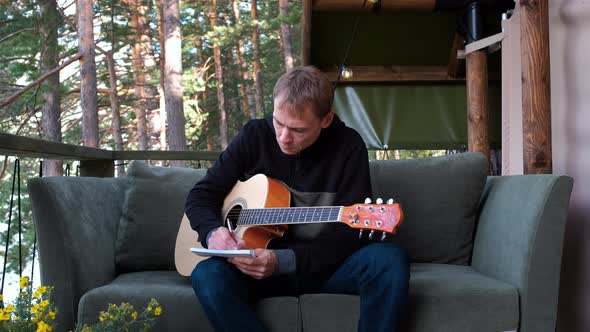 Man Playing Guitar and Writing Lyrics for Song