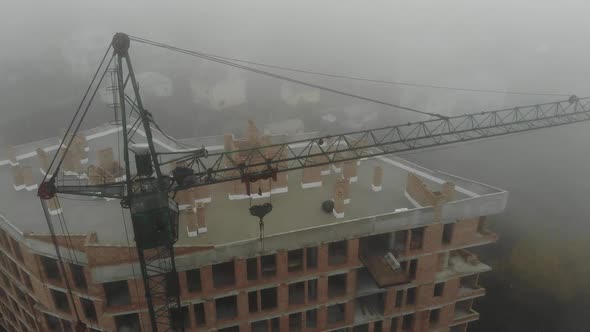 Birds eye view on tower crane in fog standing next to residential building.