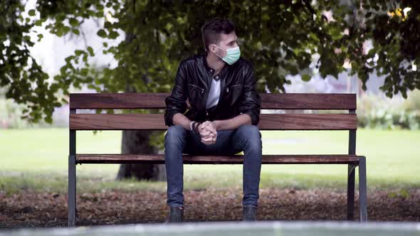 A young cool man in jeans, white T-shirt and a black leatherette jacket, wearing a green Covid-19 fa