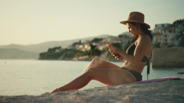 The Girl Sprays and Spreads Sunscreen on the Body By the Ocean