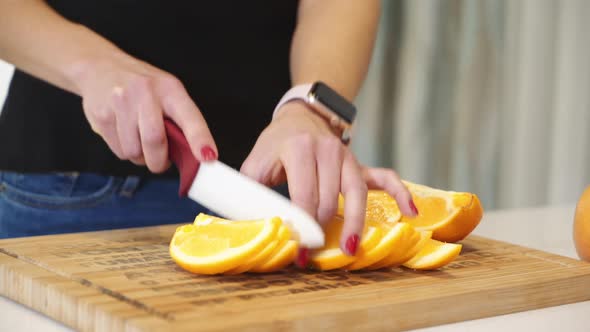 Female hands cutting orange on a wooden board. Woman in the kitchen. Healthy eating. Raw food.