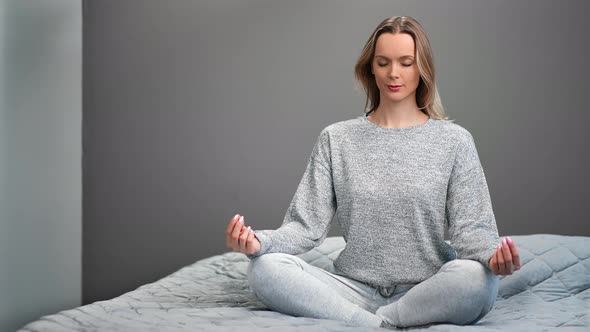 Happy Woman with Closed Eyes Sitting on Bed in Lotus Position