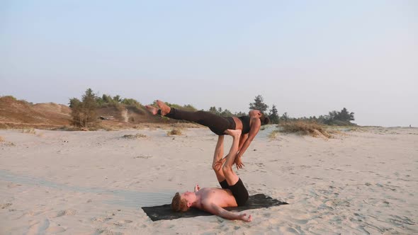 Fit Sporty Couple Practicing Acro Yoga with Partner Together on the Sandy Beach