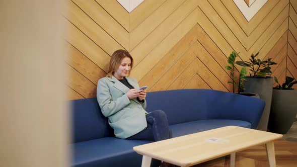 Happy young woman using smartphone while sitting on a sofa at lobby hotel.