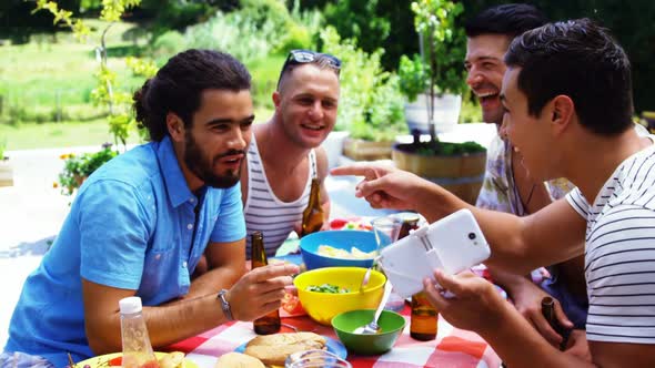 Smiling man showing his mobile phone to his friends while having meal outdoors